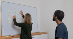 A female academic writing on post it notes on a white board in collaboration with a male colleague