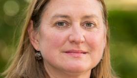 Photo of Juliet Dryden who is a white woman with mid-length brown hair on a blurred green background.