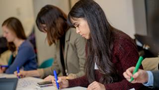 three girls with brown hair looking down and writing on paper