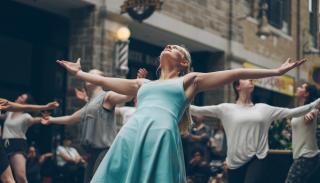 female actor in a blue dress with arms outstretched