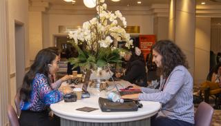 A group of women PhD students working at a table with a large vase of white flowers on it