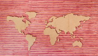 A wooden cut out of the world map on a pink and red striped background