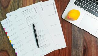 papers and corner of a laptop on a wooden desk