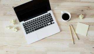 wooden table with a laptop, mug of black coffee and some pencils on top