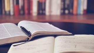two books laying open on a desk with library shelves in the background
