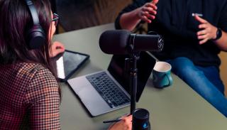 Two people with headphones on leaning over a podcast microphone