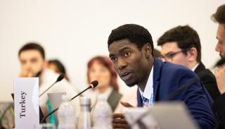 A student in a suit speaking at the 2024 BISA climate simulation