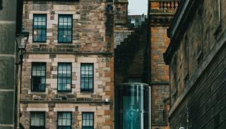 A road leading to with brown brick buildings one of which has a Scottish flag