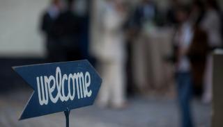 A welcome sign in the foreground with a blurred group of people behind