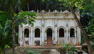 A UNSECO heritage site of an old white building with 5 large windows situated in a forest with greenery surrounding it