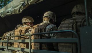 Soldiers dressed in camouflage lined up with their backs to the camera seated in a military truck with a green awning