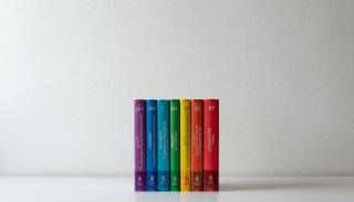 A row of books in a rainbow against a white wall