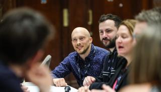 Nick Caddick in a blue shirt talking to colleagues at a roundtable