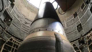 A large rocket capsule standing vertically inside an industrial test chamber, viewed from below.