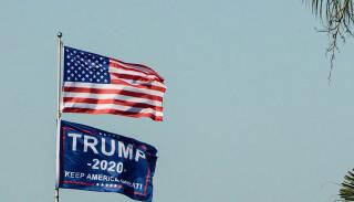 an American flag and Trump flag flying in front of a nice blue sky