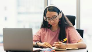 A female student wearing headphones and studying with a laptop