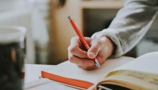 a hand holding a pen, writing in a notebook