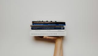 Hand holding a stack of books up in the air 
