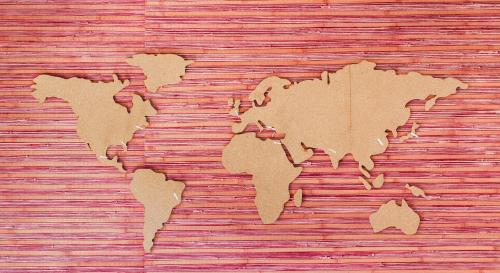 A wooden cut out of the world map on a pink and red striped background