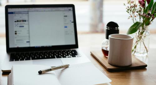 piece of paper with pen laying next to it and a laptop behind it
