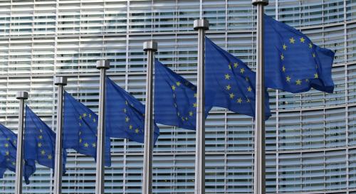 7 EU flags in a row in front of a windowed building 