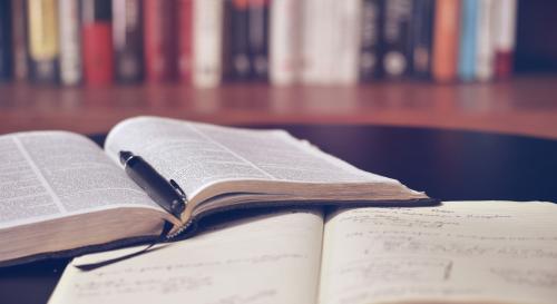 two books laying open on a desk with library shelves in the background