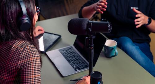 Two people with headphones on leaning over a podcast microphone