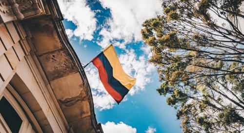 Colombian flag coming off a building against a blue cloudy sky and through trees