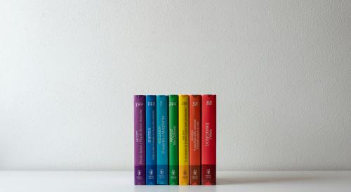 A row of books in a rainbow against a white wall
