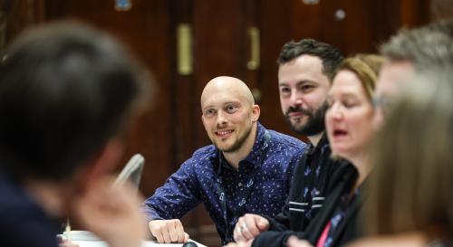 Nick Caddick in a blue shirt talking to colleagues at a roundtable