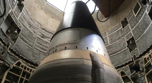 A large rocket capsule standing vertically inside an industrial test chamber, viewed from below.