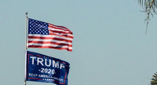 an American flag and Trump flag flying in front of a nice blue sky