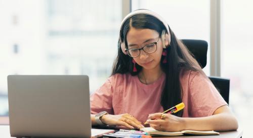 A female student wearing headphones and studying with a laptop
