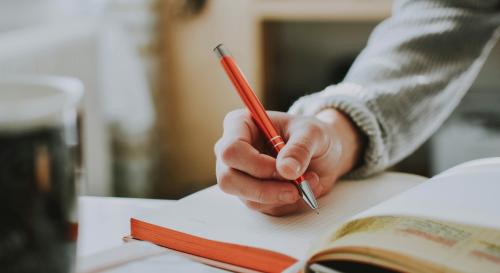 a hand holding a pen, writing in a notebook