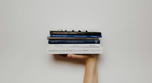 Hand holding a stack of books up in the air 